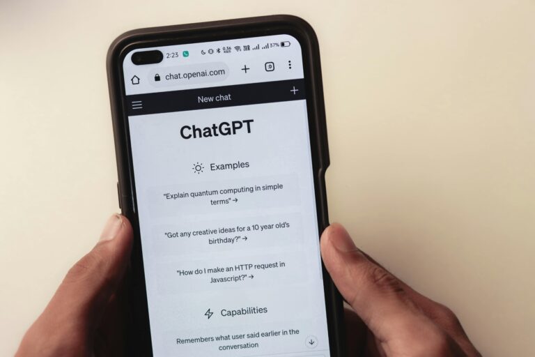 Pessoa segura um smartphone exibindo a interface do ChatGPT na página inicial, com exemplos de perguntas como “Explain quantum computing in simple terms” e uma seção de funcionalidades visíveis, representando o início de uma conversa onde o recurso “Refletir” pode ser utilizado.