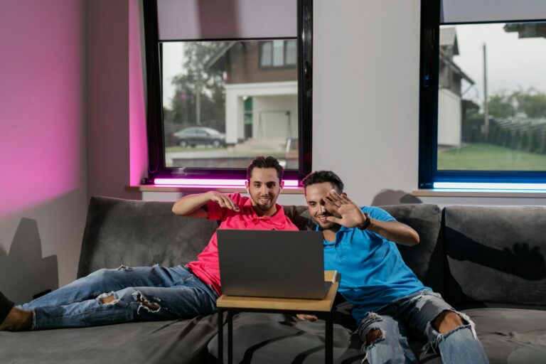 Dois homens sorrindo e interagindo com um notebook em ambiente doméstico, simbolizando a interatividade e sincronização típica de gêmeos digitais.