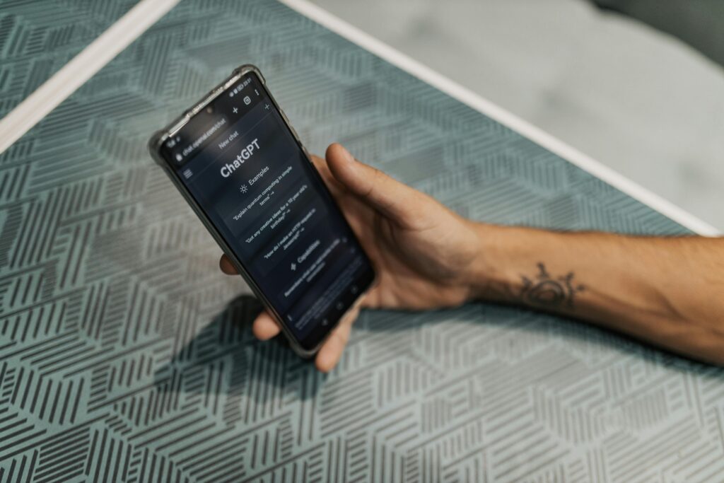 Pessoa segurando smartphone com a interface do ChatGPT aberta, representando o uso de inteligência artificial generativa na criação de conteúdos por meio de assistentes virtuais.