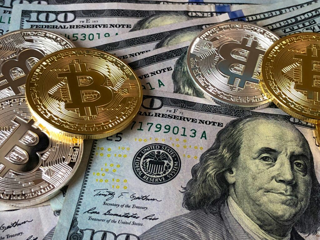 Moedas de Bitcoin sobre cédulas de dólar, representando a conexão entre Blockchain, criptomoedas e o sistema financeiro global.
