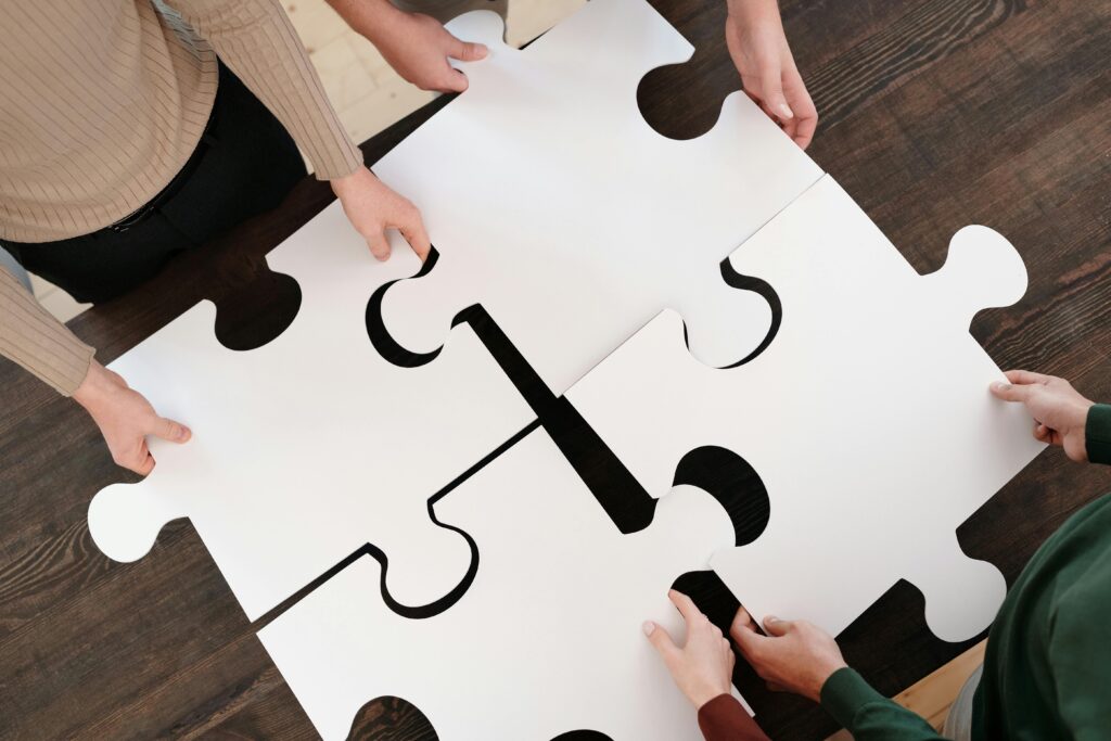 Quatro pessoas colaboram montando peças de um grande quebra-cabeça branco sobre uma mesa de madeira escura, representando a validação de uma solução para um problema específico.
