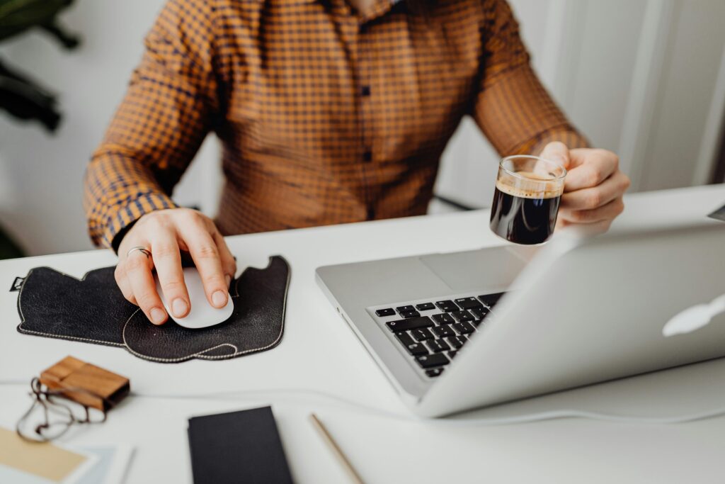 Profissional trabalhando em notebook com café em mãos, representando a agilidade, portabilidade e leveza no desenvolvimento de aplicações através do uso de containers como o Docker.