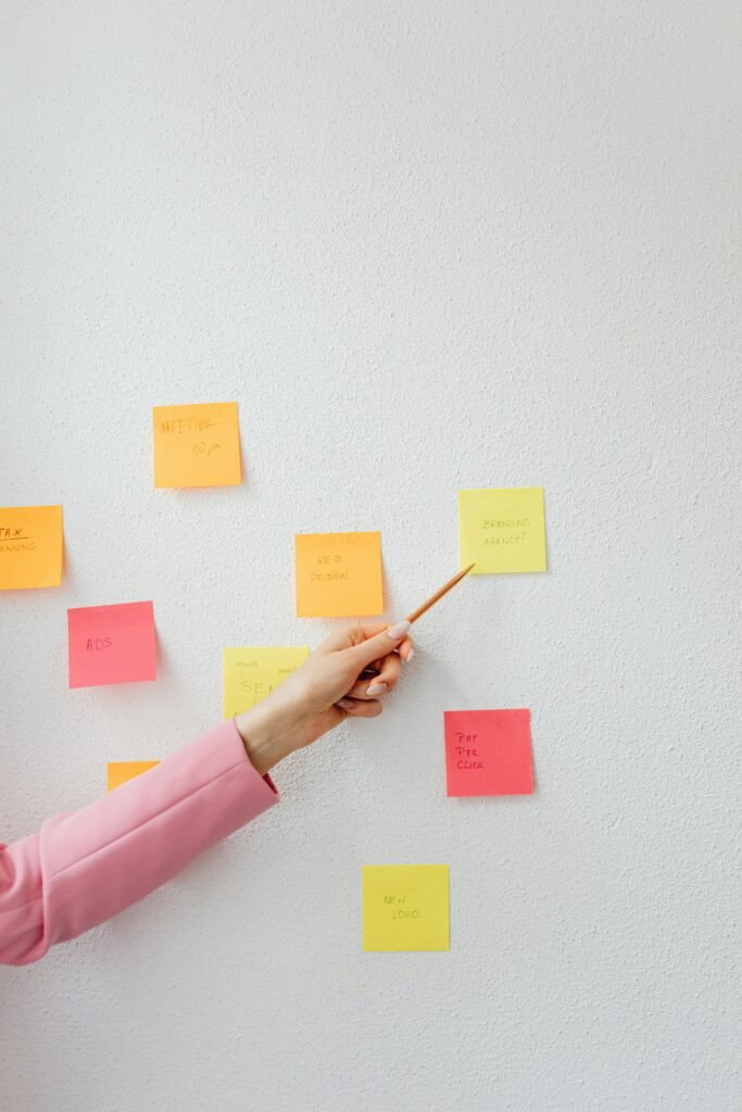 Pessoa apontando para post-its coloridos organizados em um quadro branco, representando a metodologia Kanban de gestão visual de tarefas e fluxo de trabalho.