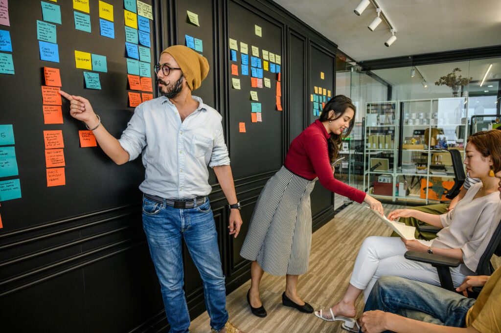 Equipe ágil em reunião de planejamento utilizando post-its em quadro de tarefas, representando a metodologia Scrum aplicada à gestão de projetos e desenvolvimento de produtos.