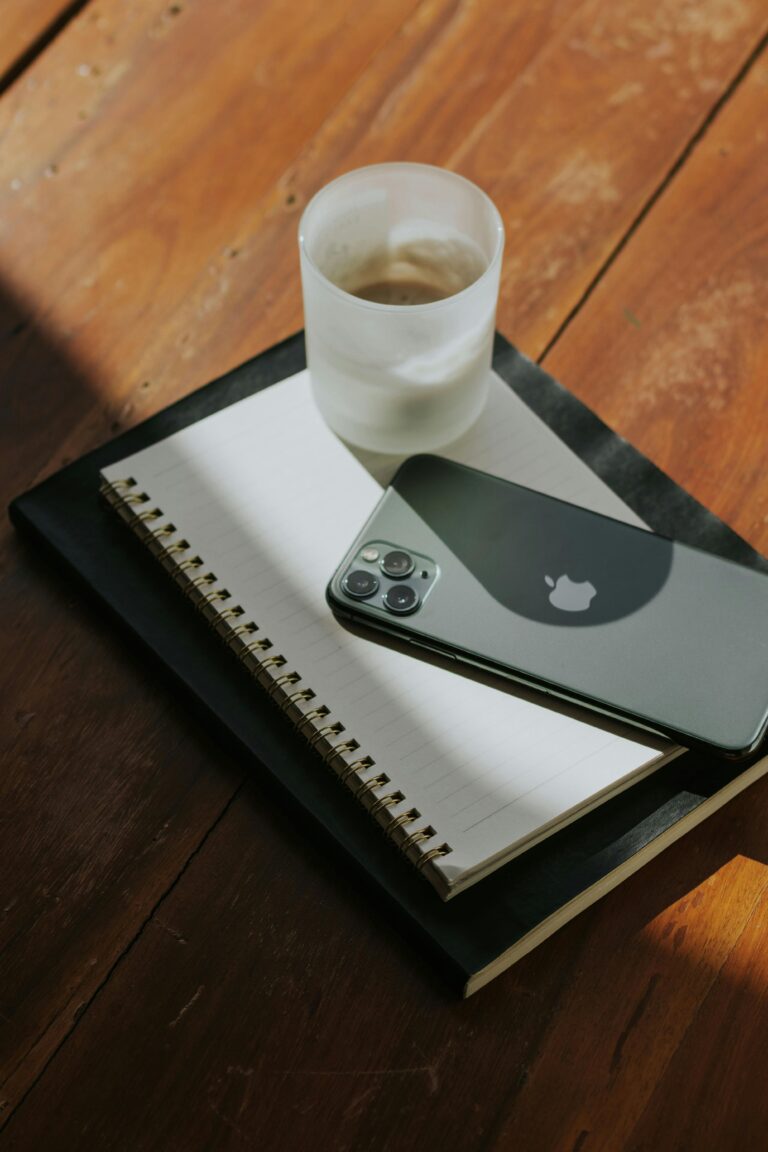 Notebook, caderno e smartphone sobre uma mesa de madeira, representando a documentação e organização de Release Notes no desenvolvimento de produtos digitais.