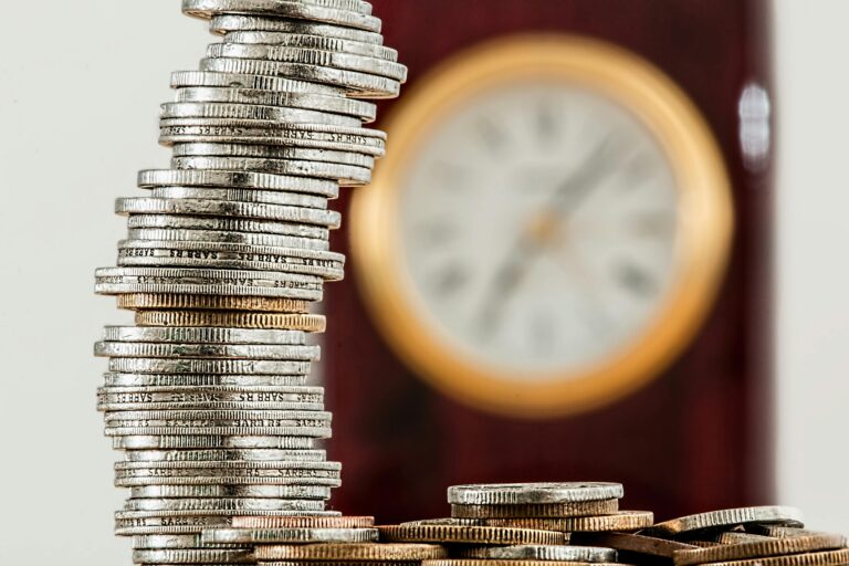Pilha instável de moedas com relógio ao fundo, simbolizando a dívida técnica em projetos digitais e a relação entre custo, tempo e manutenção de software.