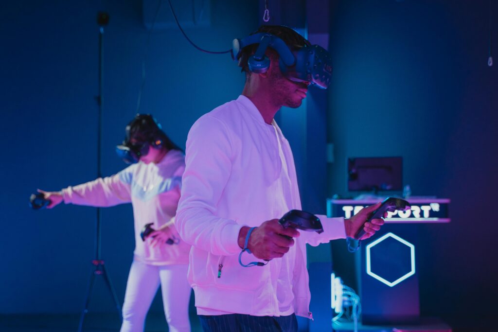 Duas pessoas utilizando headsets de realidade virtual e controles manuais em ambiente neon, demonstrando imersão no metaverso.