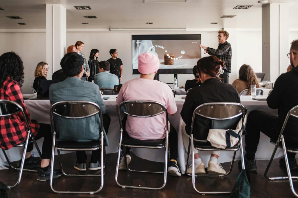 Equipe assistindo a apresentação sobre UX Design em sala de workshop, com foco em experiência do usuário e prototipagem de interfaces digitais.