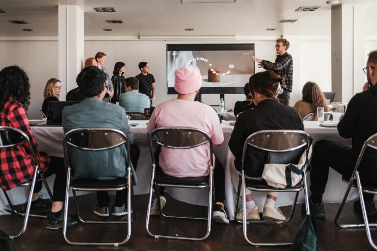 Equipe assistindo a apresentação sobre UX Design em sala de workshop, com foco em experiência do usuário e prototipagem de interfaces digitais.