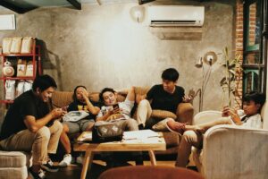 Grupo de jovens reunidos em um ambiente descontraído, interagindo com seus celulares enquanto compartilham momentos de forma espontânea e conectada, refletindo o uso intenso de redes sociais e hashtags.