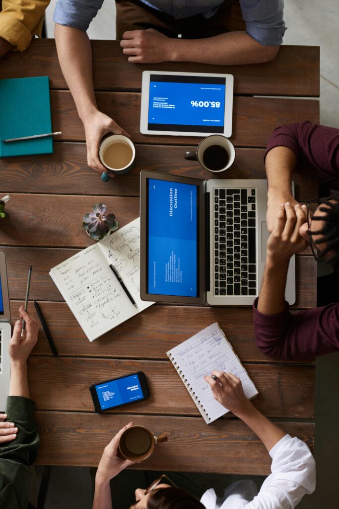 Visão aérea de uma equipe colaborando em mesa de trabalho com notebooks, tablets e anotações, representando planejamento estratégico para a criação de uma homepage.