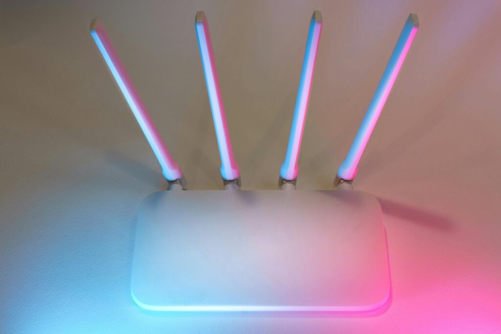 Roteador com quatro antenas iluminado por luzes neon azul e rosa, representando segurança de rede e firewall.