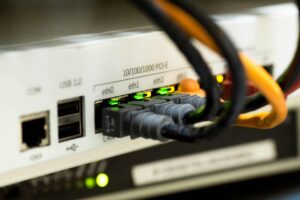 Conexões de rede com cabos ethernet conectados a um roteador ou switch, simbolizando a infraestrutura crítica de cibersegurança e proteção de dados.