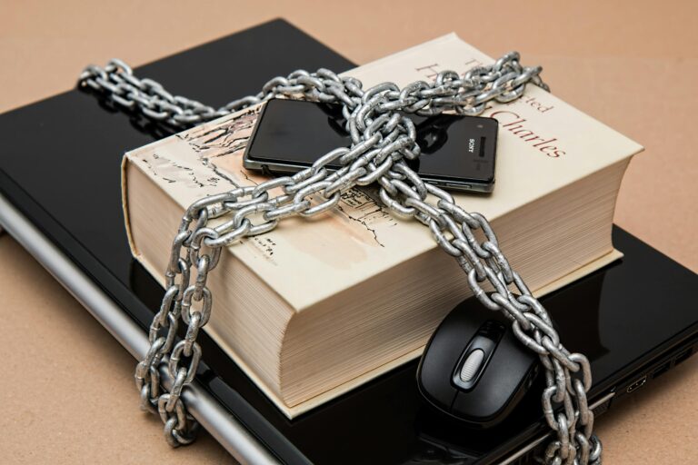 Livro, celular e notebook protegidos por correntes de metal, simbolizando a proteção de dados exigida pela LGPD.
