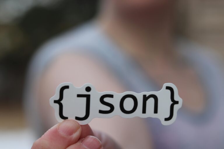 Pessoa segurando adesivo com a palavra JSON entre chaves, simbolizando a popular notação de objetos usada para troca de dados na web.
