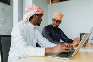Dois profissionais em trajes tradicionais trabalhando lado a lado com notebooks, trocando informações e analisando dados em um ambiente colaborativo, representando práticas seguras de download e compartilhamento digital.
