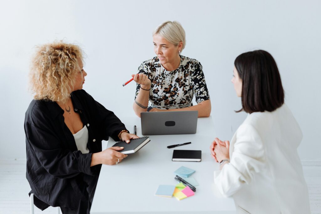 Três profissionais discutindo estratégias digitais em ambiente de escritório, com laptop e anotações sobre a mesa, ilustrando conversas sobre consentimento e uso de cookies.