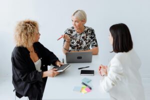 Três profissionais discutindo estratégias digitais em ambiente de escritório, com laptop e anotações sobre a mesa, ilustrando conversas sobre consentimento e uso de cookies.