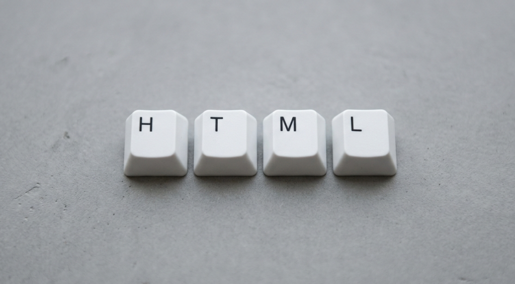 Teclas brancas formando a palavra HTML sobre fundo cinza liso, simbolizando linguagem de marcação usada na web.