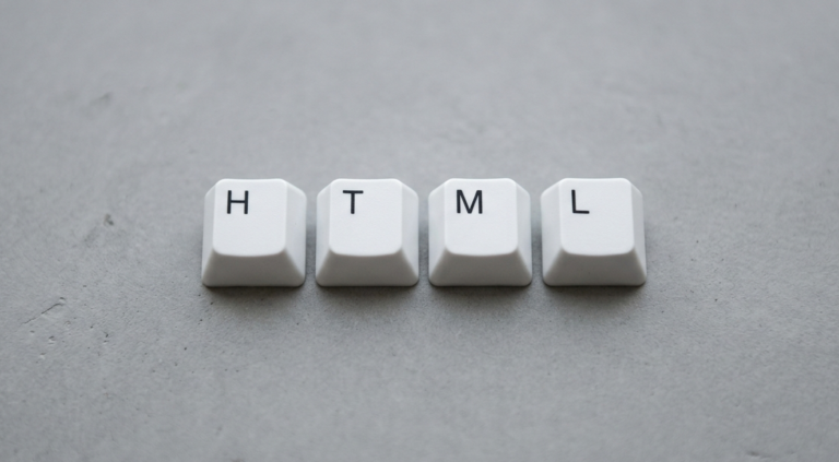 Teclas brancas formando a palavra HTML sobre fundo cinza liso, simbolizando linguagem de marcação usada na web.