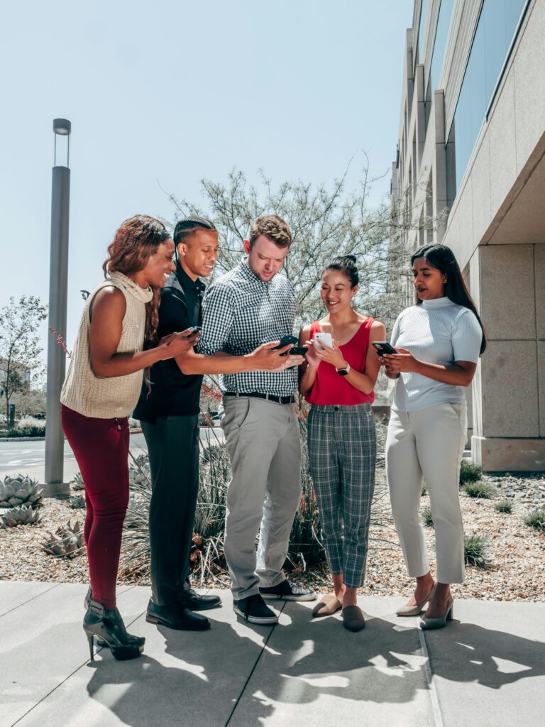 Grupo de profissionais sorrindo enquanto observam seus celulares, simbolizando o uso de inteligência artificial no ambiente corporativo moderno