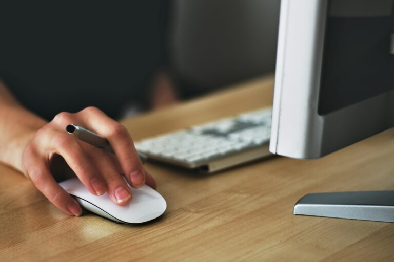 Pessoa utilizando mouse ao lado de um monitor de computador, simbolizando o uso de automação inteligente para otimizar tarefas digitais no ambiente corporativo.