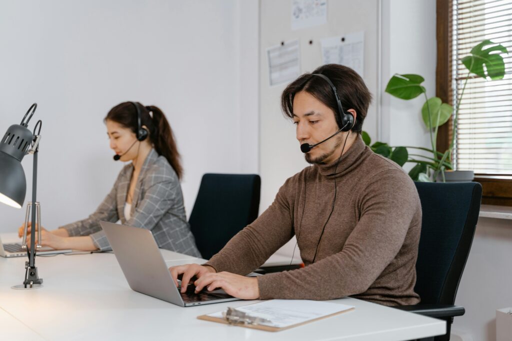Profissionais de suporte técnico utilizam notebooks com headsets em ambiente corporativo durante processo de migração de sistemas.
