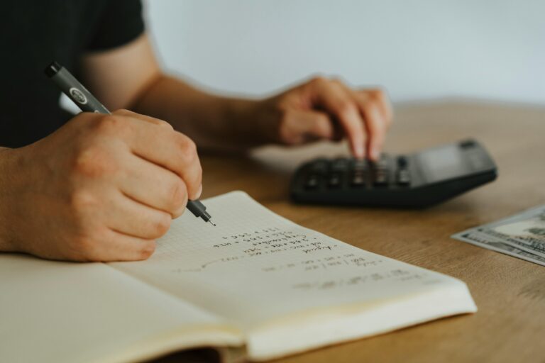 Pessoa fazendo cálculos manuais com caderno e calculadora, representando impacto da reforma tributária nos processos financeiros.
