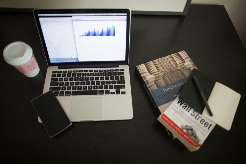 Notebook com gráficos de desempenho financeiro ao lado de livros sobre Wall Street e finanças corporativas.