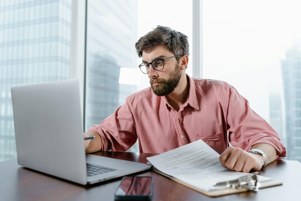 Homem analisando documentos e planilhas no notebook, refletindo sobre os impactos da reforma tributária nos sistemas da empresa.