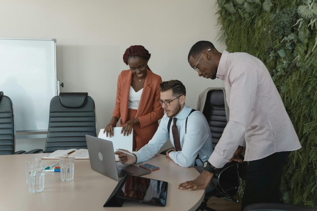 Um grupo diversificado de três profissionais de negócios colaborando ao redor de uma mesa com notebook aberto e tablet, representando a governança humana necessária para implementar sistemas de Inteligência Artificial na empresa.