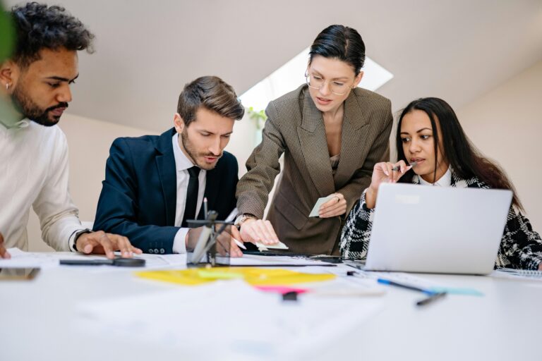 Quatro profissionais em reunião colaborativa ao redor de uma mesa com notebook, documentos e anotações, discutindo a governança de Inteligência Artificial na empresa.