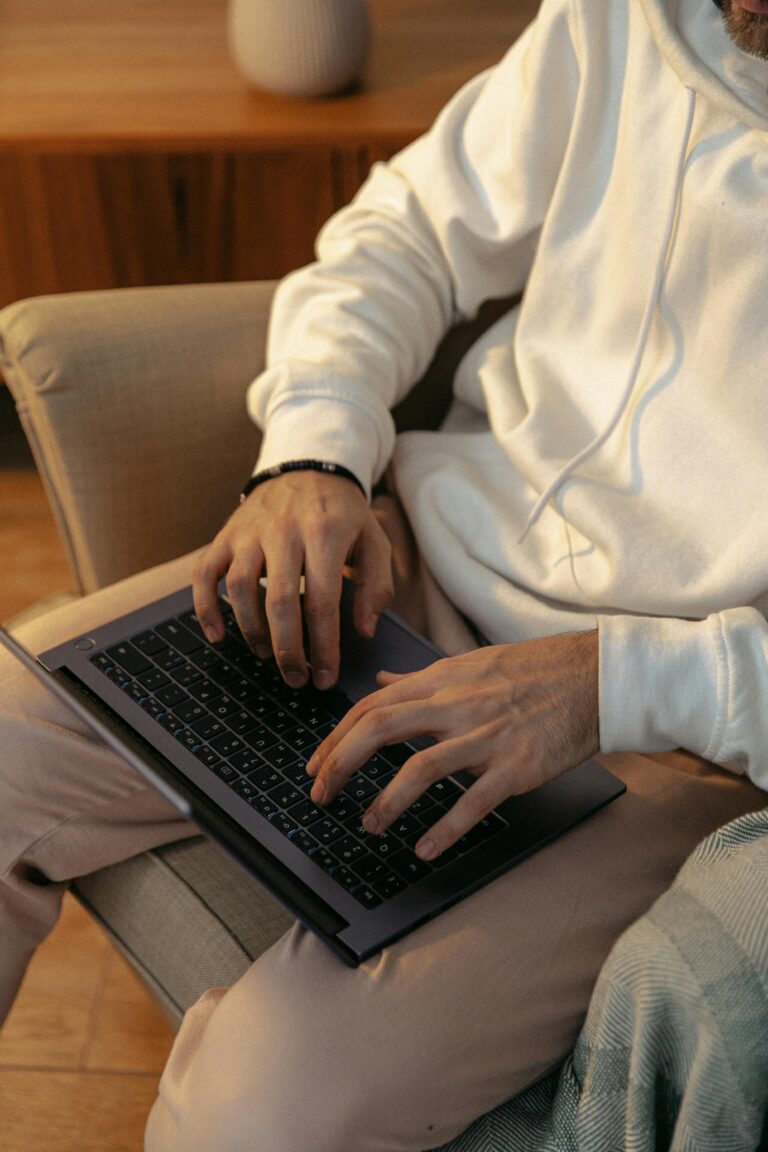 Homem sentado em uma poltrona confortável utilizando um laptop para gerenciar seu assistente pessoal de IA em um ambiente doméstico aconchegante.