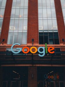 Fachada de um edifício de tijolos vermelhos e grandes janelas de vidro com o letreiro colorido do logotipo do Google em destaque na entrada.