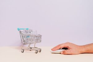Mão masculina usando mouse de computador ao lado de mini carrinho de compras com gelo, representando a inovação congelada em uma plataforma de e-commerce legada.